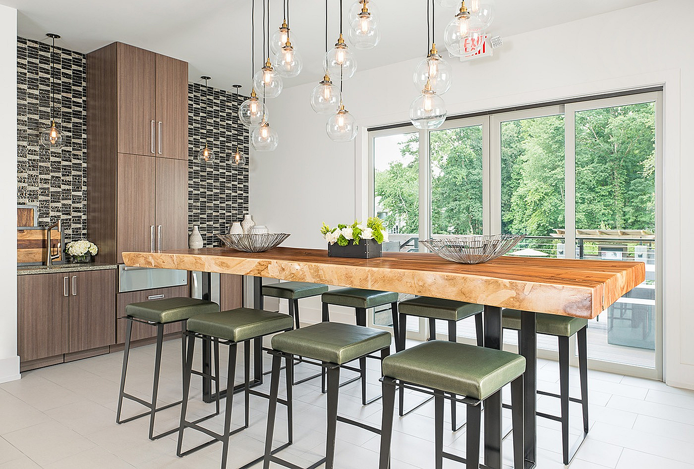 Contemporary kitchen with stylish wooden countertop, sleek pendant lighting, and lush views through expansive windows.