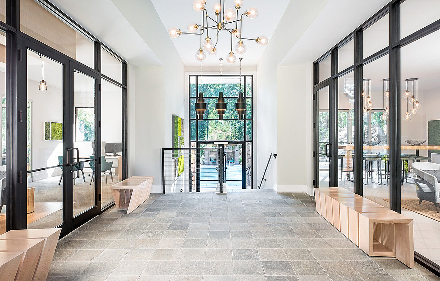 Elegant apartment lobby showcasing modern glass doors, chic lighting fixtures, and a view of a serene outdoor pool area.