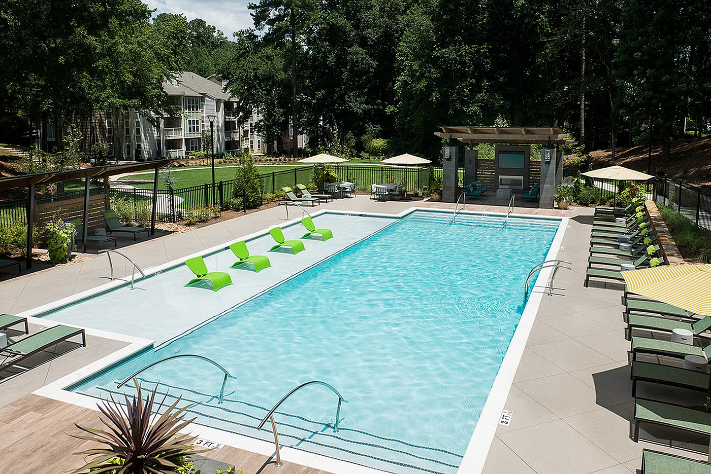 Luxurious apartment pool area featuring modern green loungers, poolside cabanas, and lush greenery for a relaxing escape.