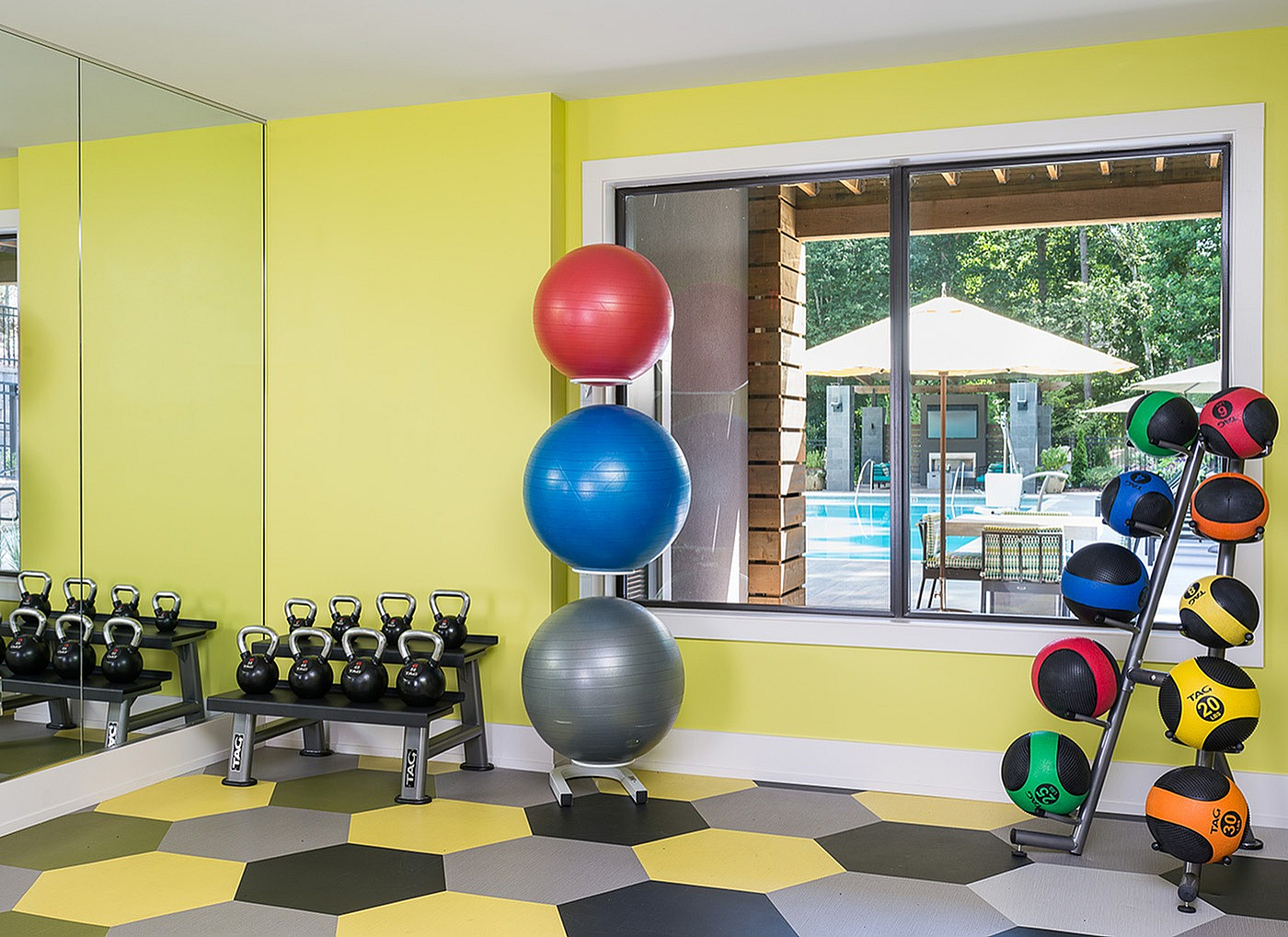Vibrant fitness room with colorful exercise balls, kettlebells, and a scenic pool view.