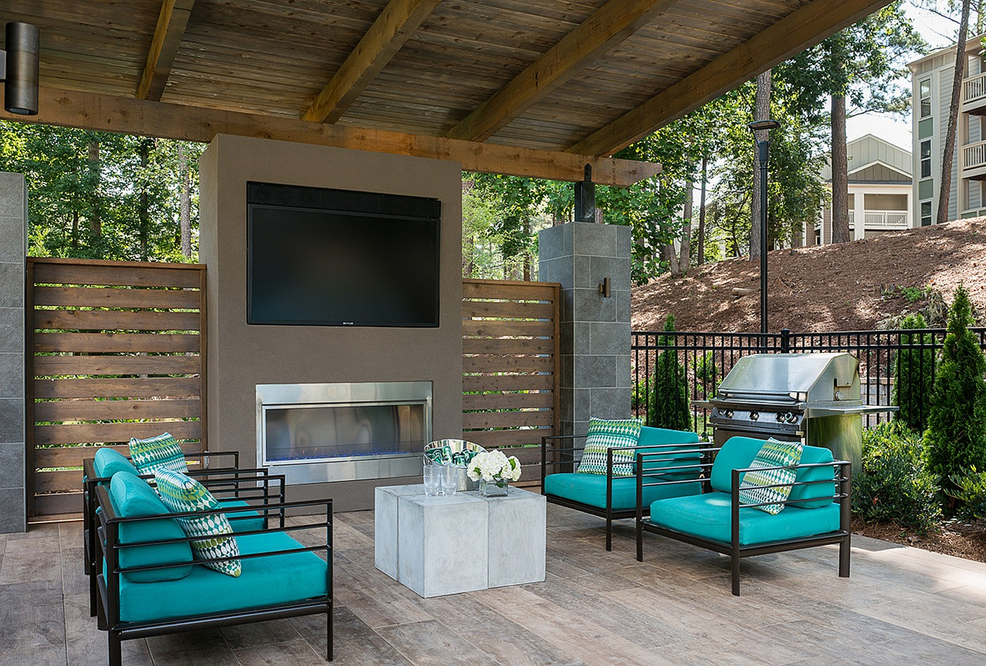 Inviting outdoor lounge featuring modern teal seating, a sleek fireplace, and a grill, perfect for entertaining in a lush, tranquil setting.