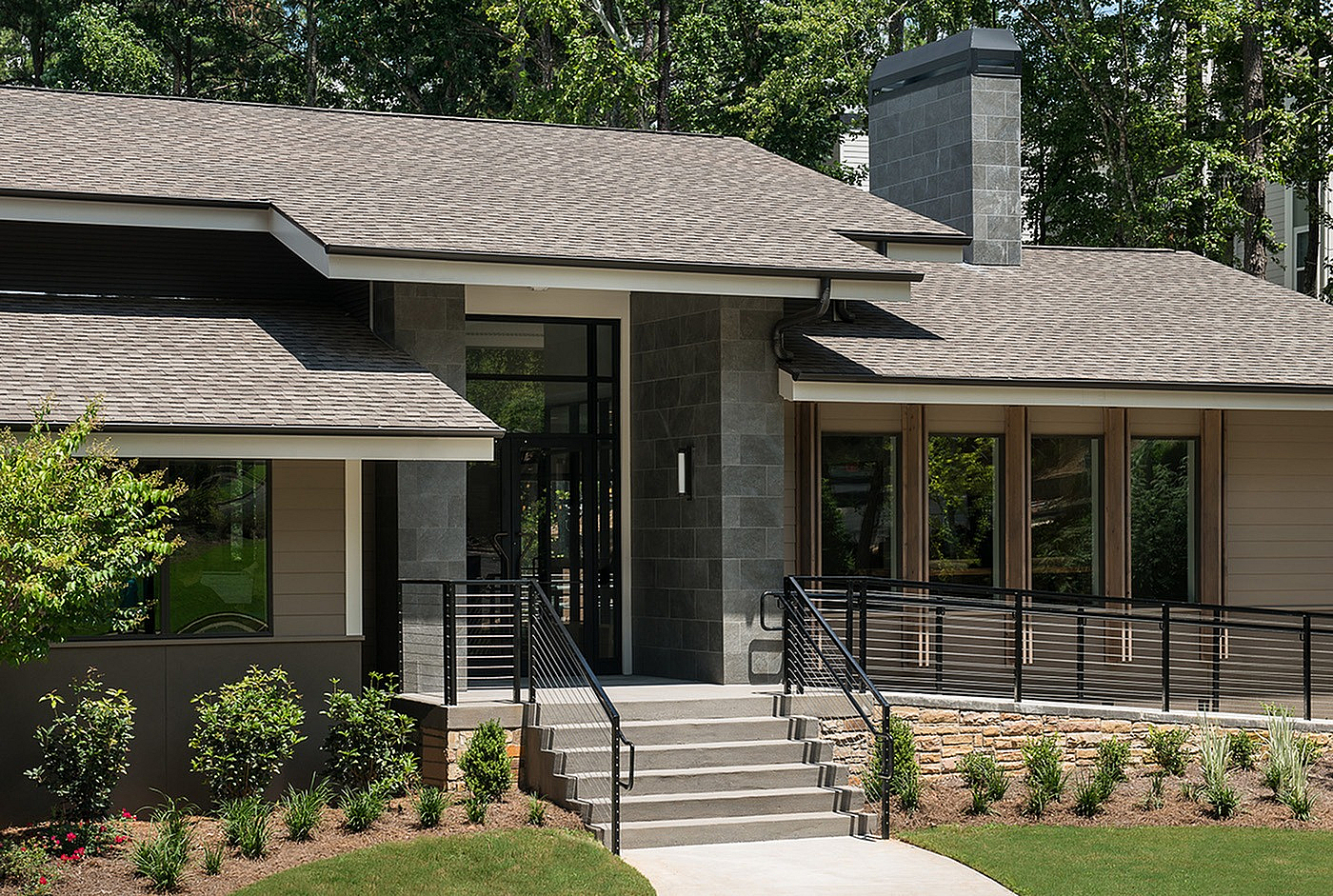 Modern home exterior with sleek stone facade and inviting entrance surrounded by lush greenery.
