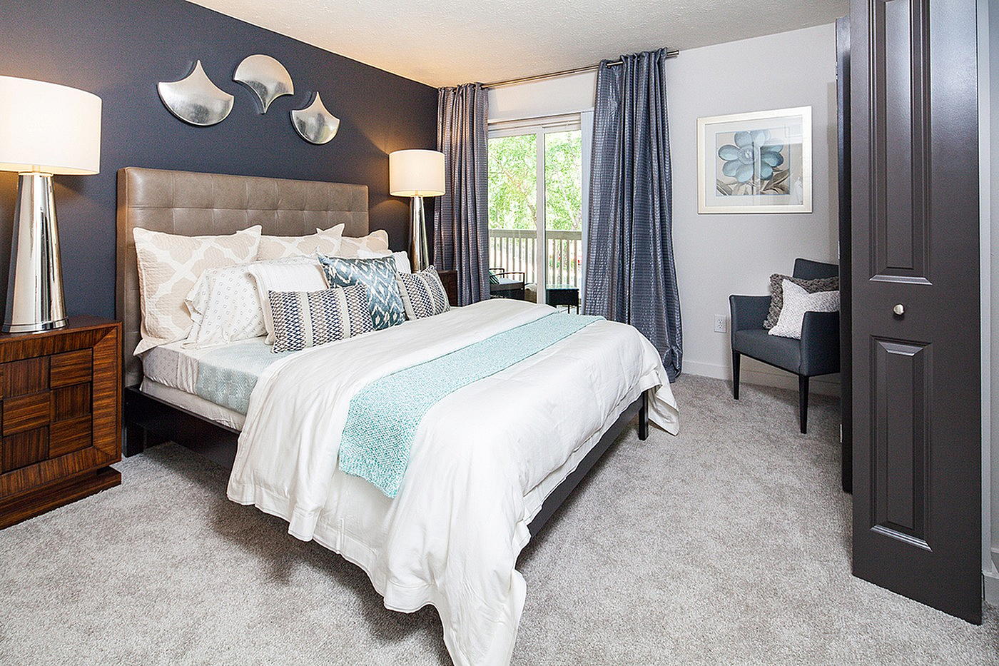 Inviting bedroom with elegant decor featuring a plush bed, stylish cushions, and contemporary art; brightened by natural light from large windows and complemented by modern lighting fixtures.