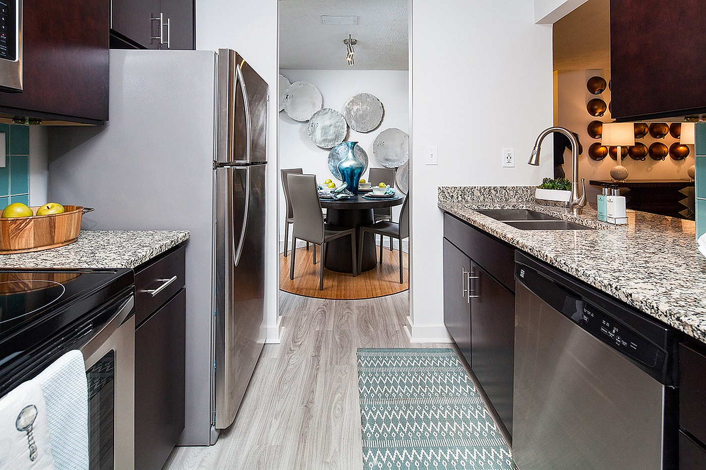 Modern kitchen with sleek stainless steel appliances and elegant granite countertops, leading to a stylishly decorated dining area with unique wall art.