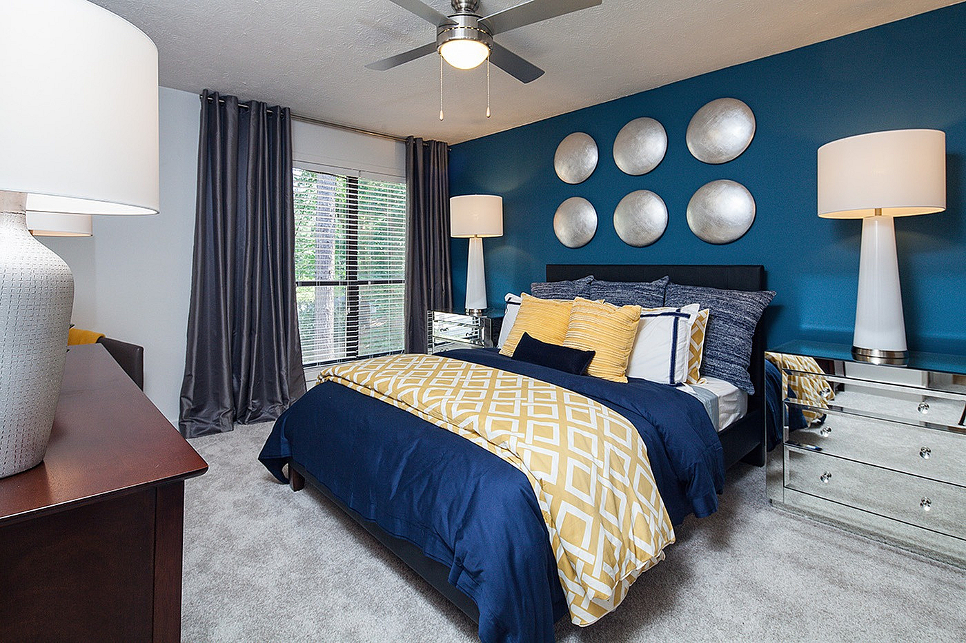 Modern bedroom with stylish blue and yellow decor, featuring elegant wall accents, luxurious bedding, and mirrored furniture.
