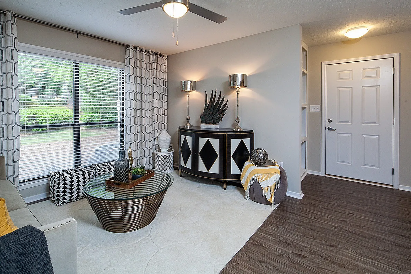 Chic living room with modern decor, featuring large window with geometric curtains, elegant sideboard, and stylish glass coffee table on plush rug.