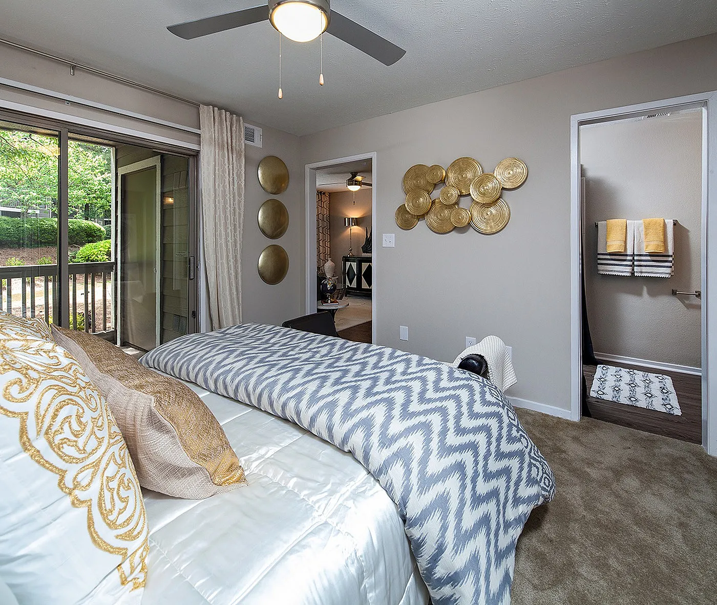 Elegant bedroom with chevron-patterned bedding, stylish wall decor, and access to scenic balcony views, leading to a modern bathroom and cozy living area.
