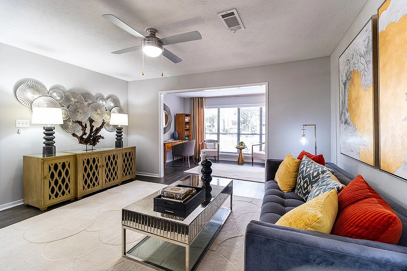Contemporary living room with chic decor, featuring a plush sofa with colorful cushions, elegant art pieces, and a stylish ceiling fan.