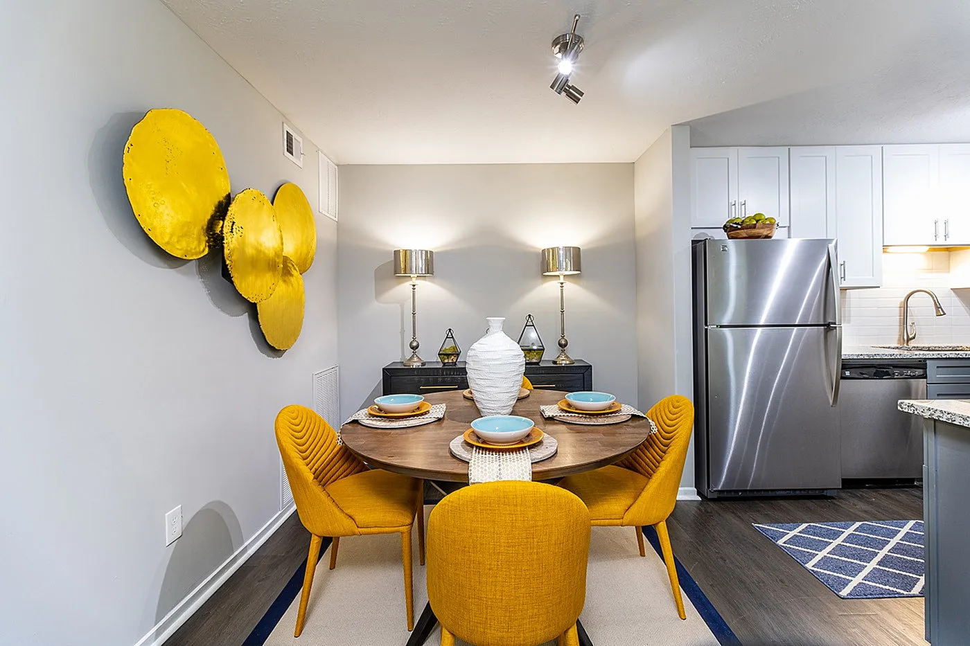 Chic dining area with vibrant yellow chairs and modern decor, next to a sleek stainless steel kitchen in a stylish apartment.