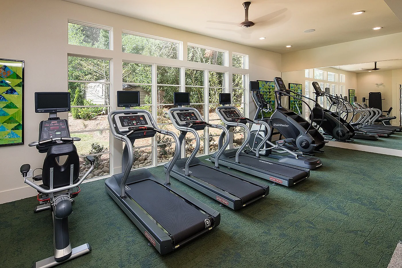 Bright, modern fitness center equipped with state-of-the-art treadmills and elliptical trainers, featuring large windows and lush outdoor views.