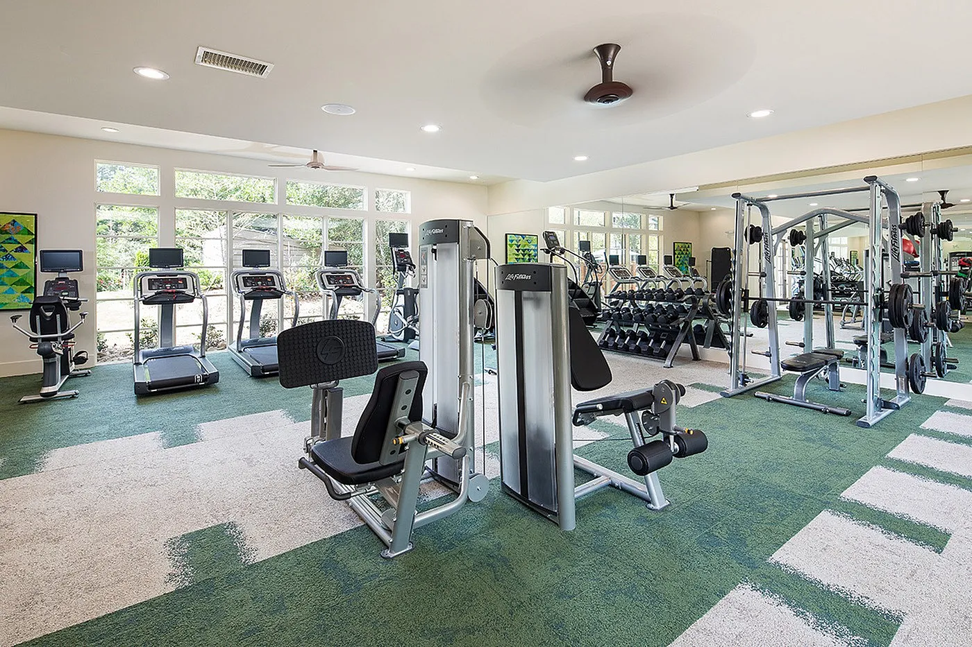 Bright and inviting fitness center with modern exercise equipment, featuring treadmills, weight machines, and a mirrored wall for a sleek, open feel.