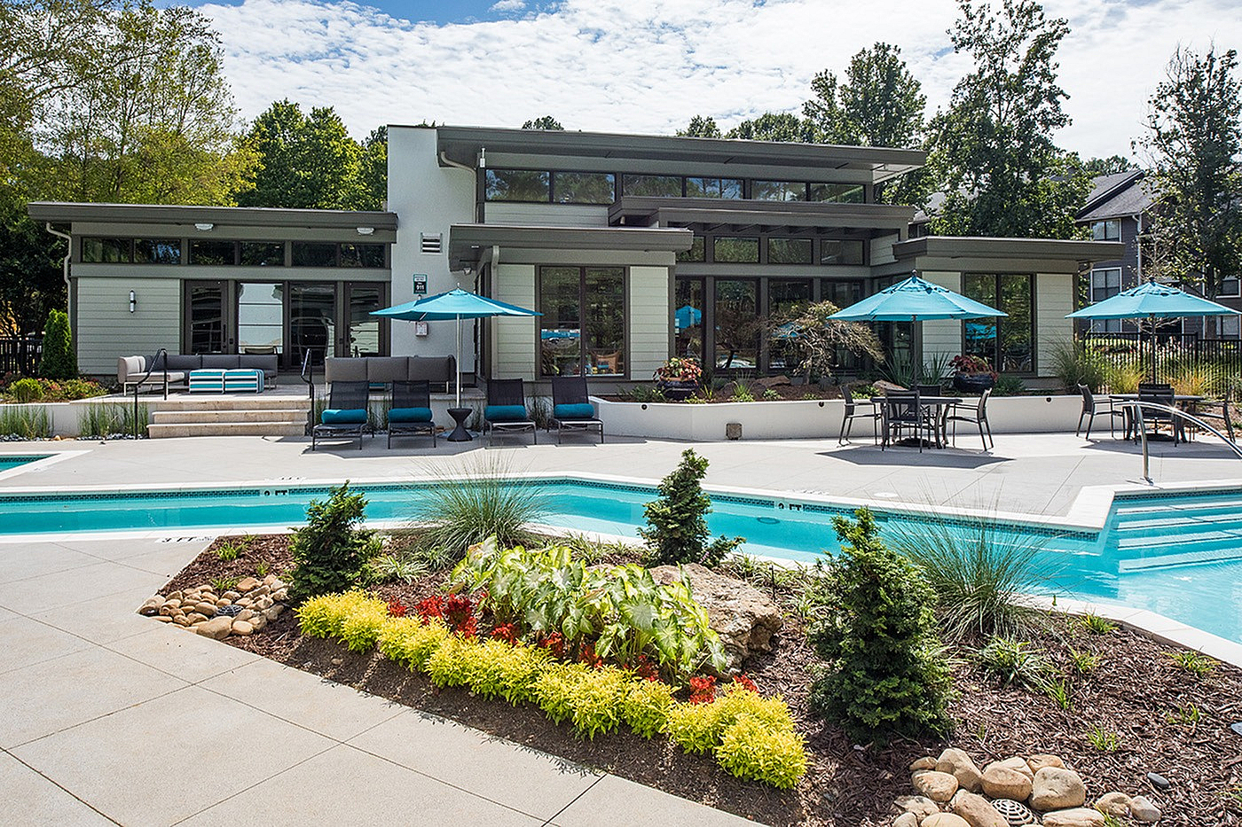 Luxurious apartment complex with a modern poolside, elegant outdoor seating, and vibrant landscaping under a clear sky.