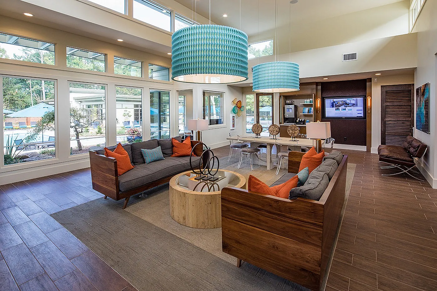 Inviting modern living room with large windows, stylish wood furniture, colorful cushions, and chic lighting, overlooking a serene outdoor pool area.