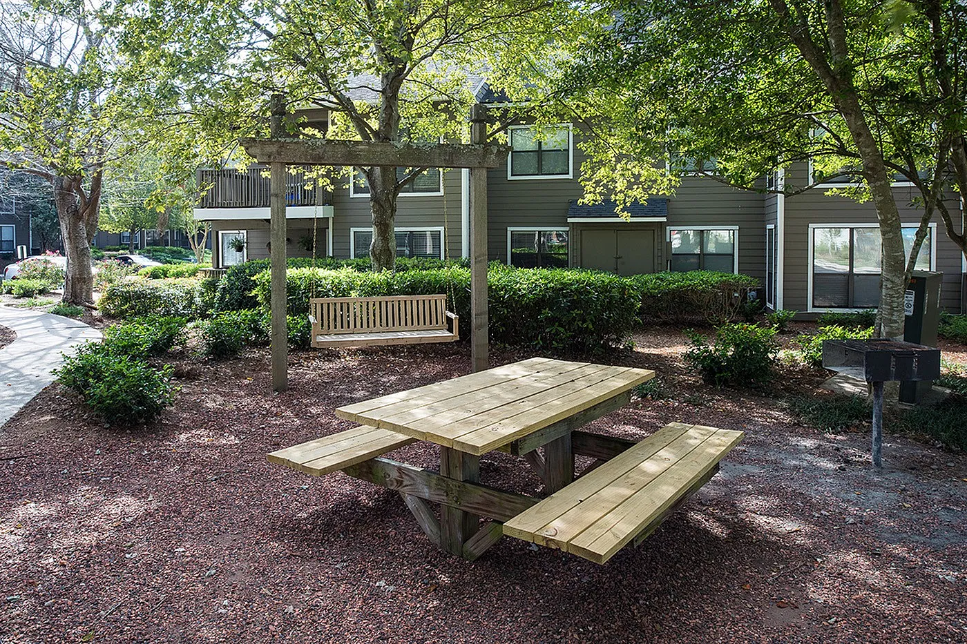 Charming outdoor area featuring a wooden picnic table and a cozy swing bench under the shade of lush green trees, perfect for relaxation and gatherings.