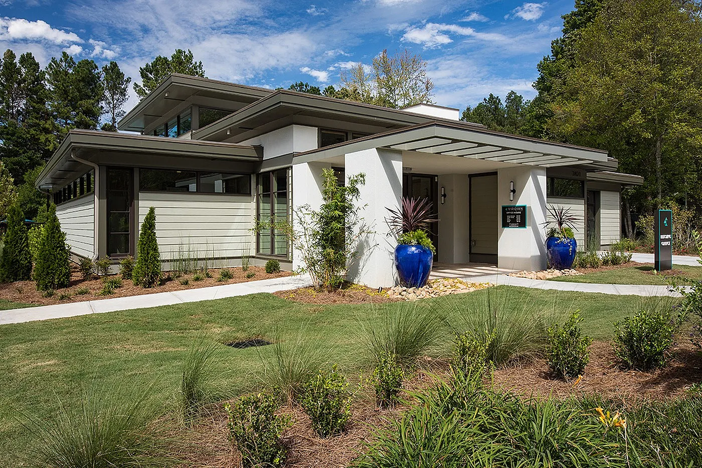 Modern home with sleek architecture, lush landscaping, and vibrant blue planters, set against a clear sky and surrounded by greenery.
