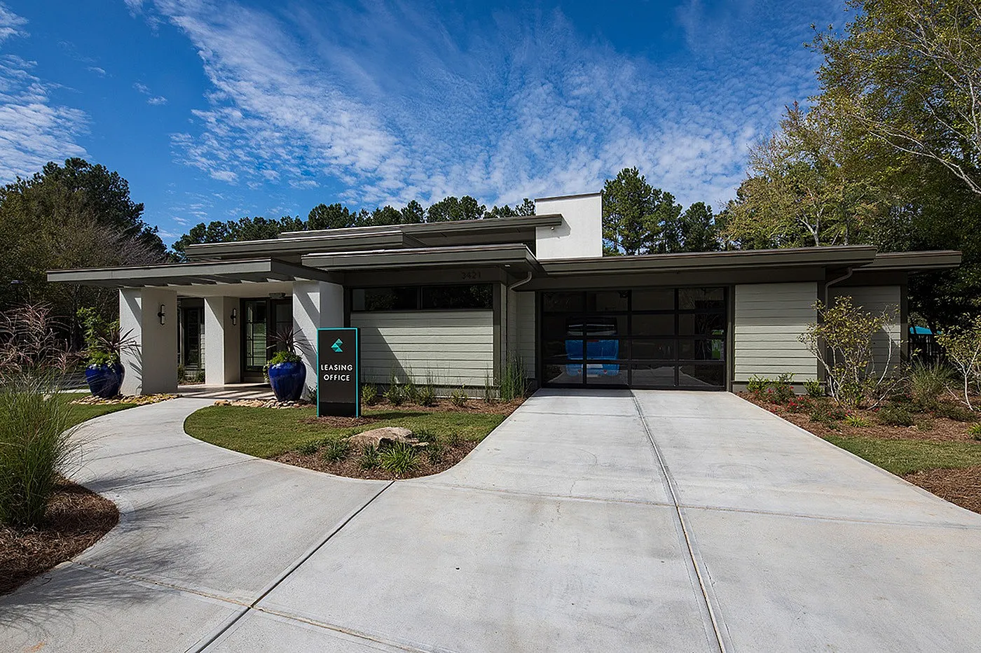 Charming and inviting leasing office with modern design, surrounded by lush greenery and a beautifully paved walkway.