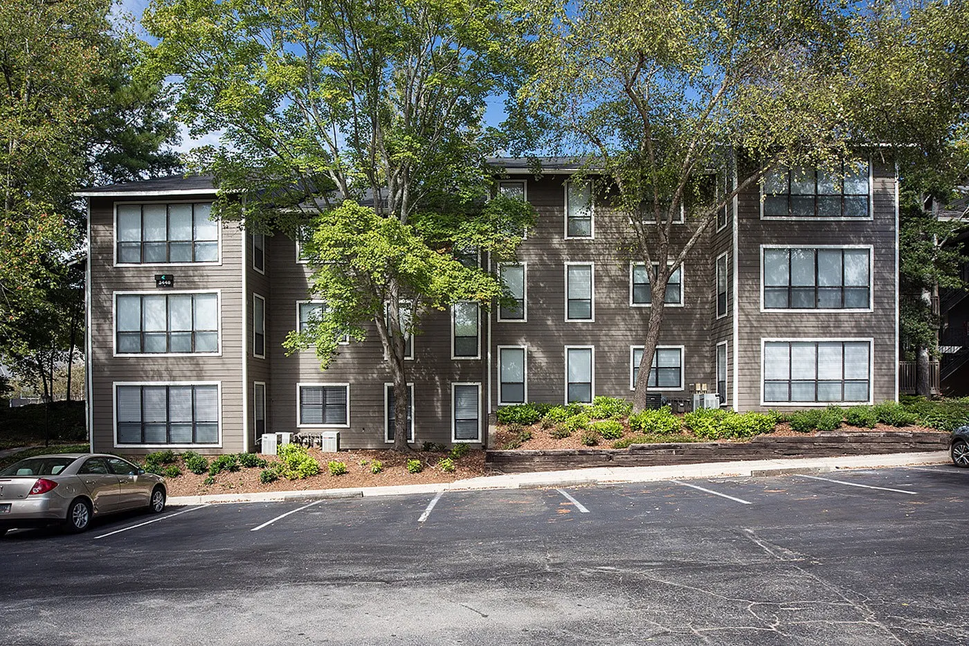 Charming apartment building surrounded by lush greenery and ample parking space, perfect for modern living.