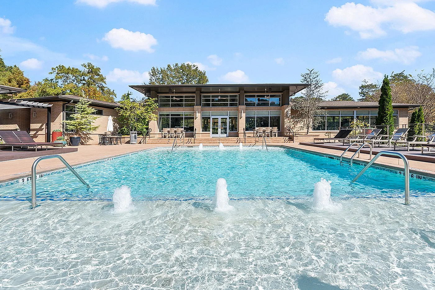 Elegant swimming pool area with crystal clear water and inviting sun loungers, set against a modern building and vibrant greenery.