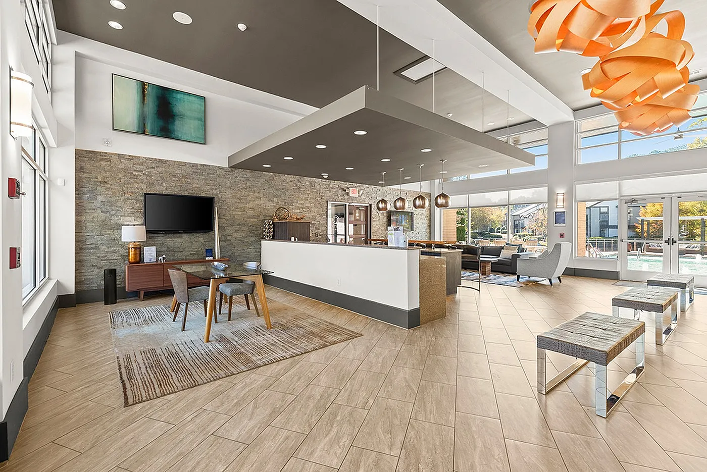 Spacious and modern lobby featuring sleek lighting, cozy seating areas, and a large TV, with natural light streaming through expansive windows.