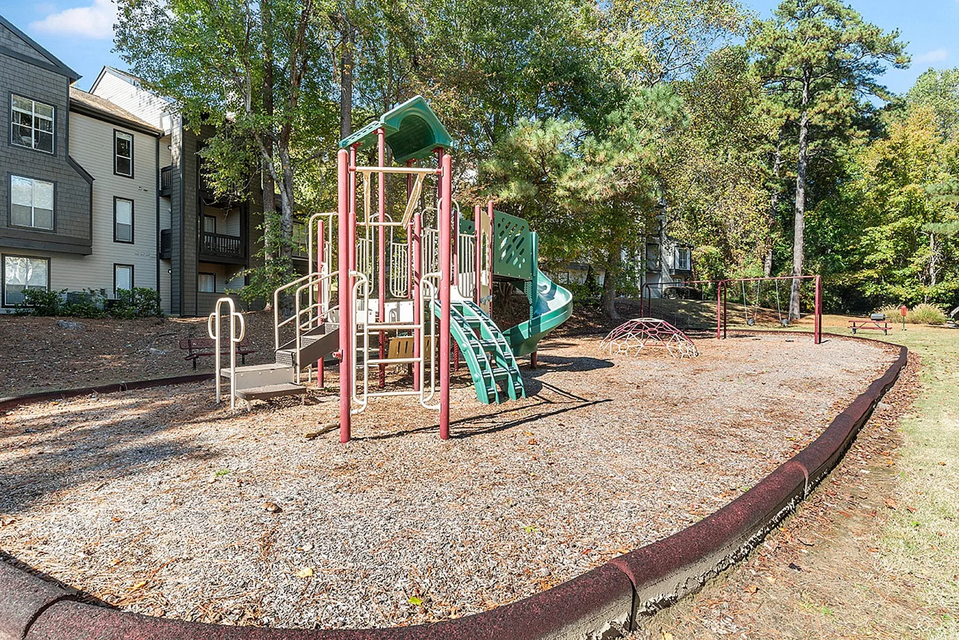 Inviting playground nestled in a serene apartment community, featuring a vibrant play structure surrounded by lush trees and well-maintained grounds.