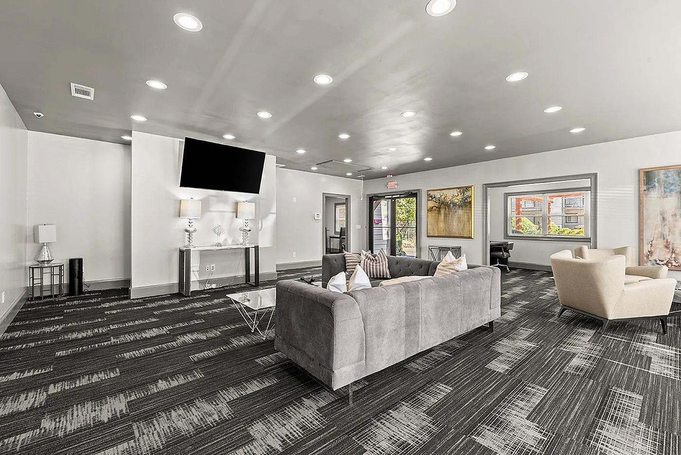 Elegant communal living area with a modern gray sofa, stylish accent chairs, and a large flat-screen TV, accented by contemporary decor and ample lighting.