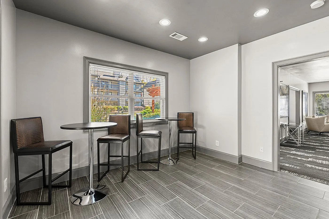 Elegant modern seating area with high stools and tables, featuring large windows and sleek gray tile flooring, perfect for casual gatherings.