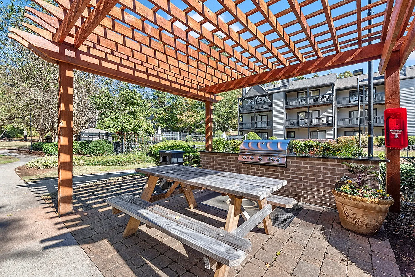 Charming outdoor space showcasing a wooden pergola, rustic picnic table, and modern grill, perfect for leisurely gatherings.