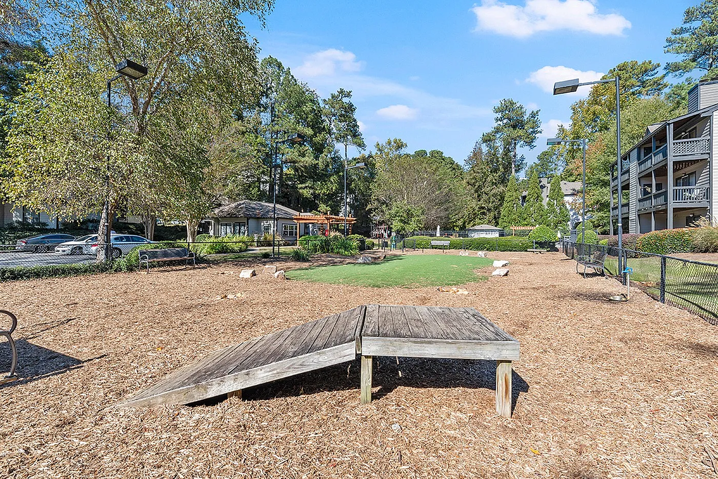 Inviting community park area with manicured green space, shaded seating, and natural wood play equipment, perfect for family enjoyment.