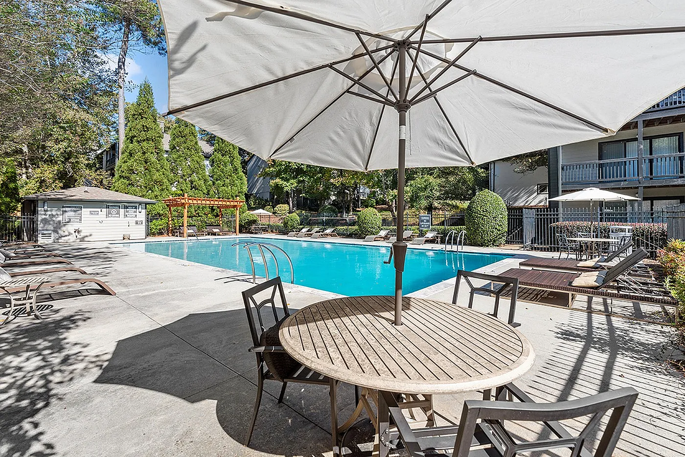 Inviting pool area with modern sun loungers, shaded seating, and lush greenery, perfect for relaxation and leisure.