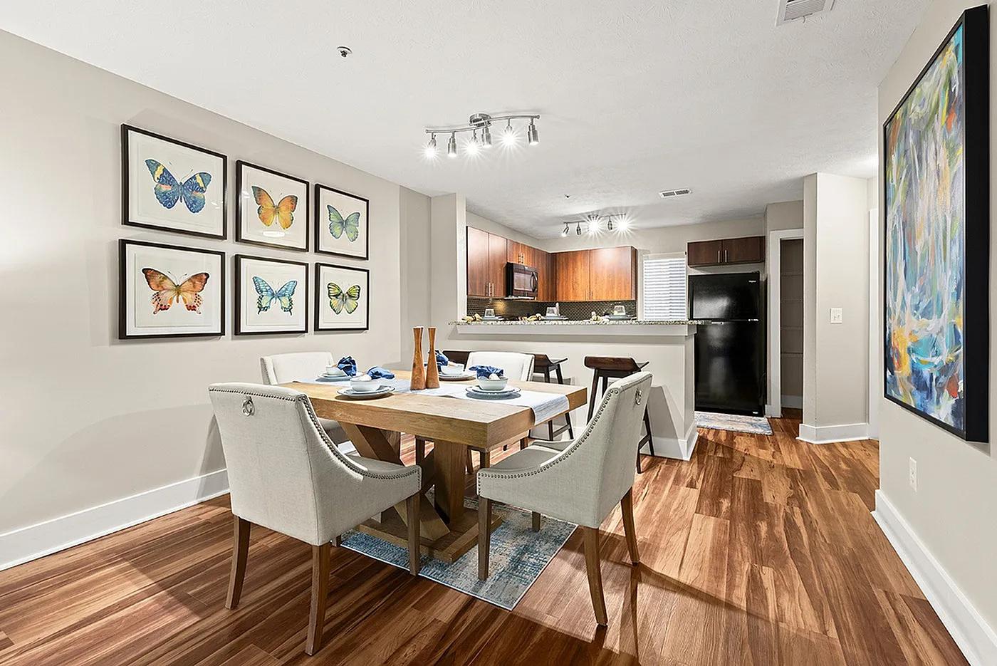 Elegant open-concept dining and kitchen area with stylish butterfly art and modern lighting, featuring a cozy dining table and sleek wooden flooring.