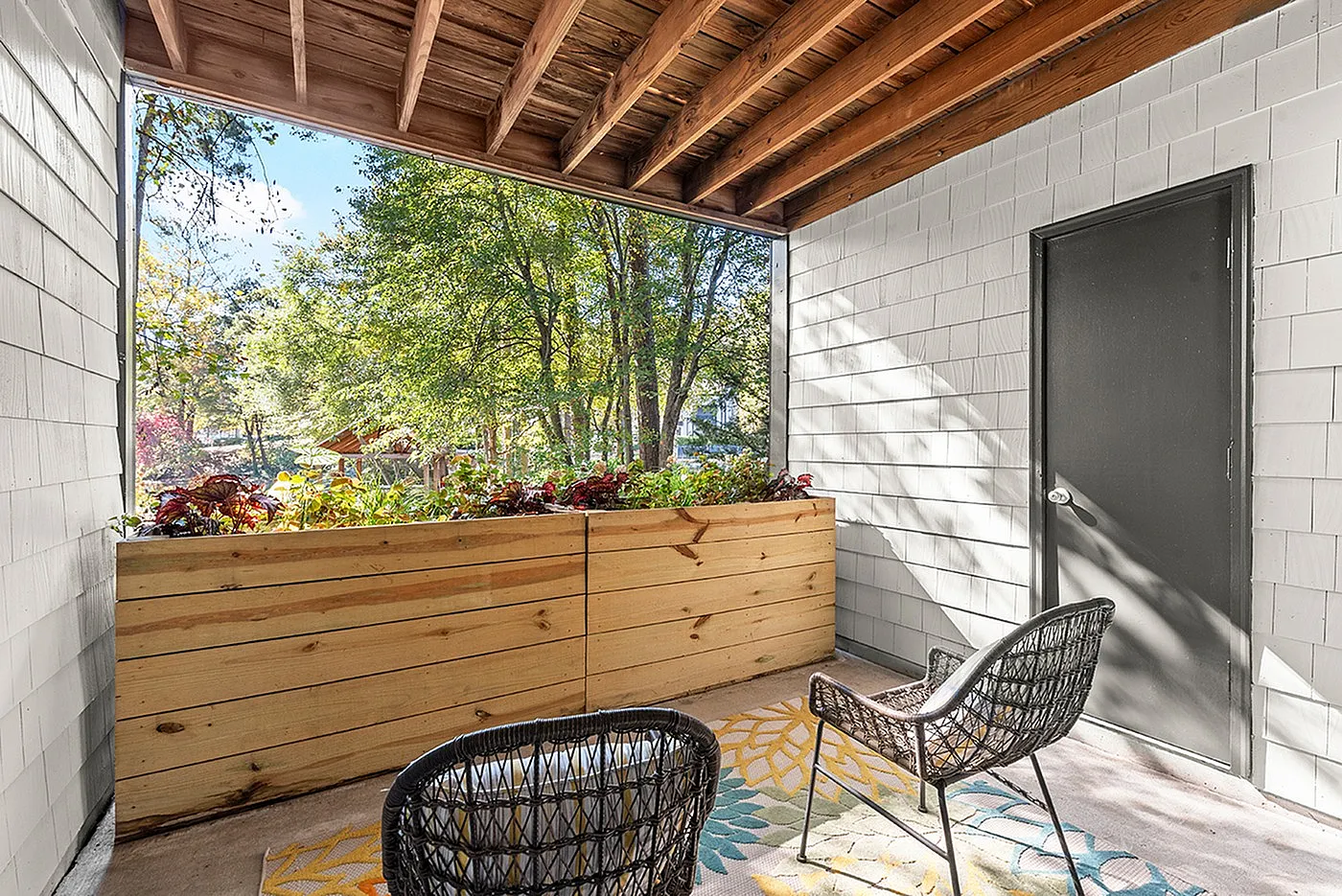 Charming outdoor balcony with woven chairs, vibrant wooden planter, and lush green view, ideal for relaxing and enjoying nature.
