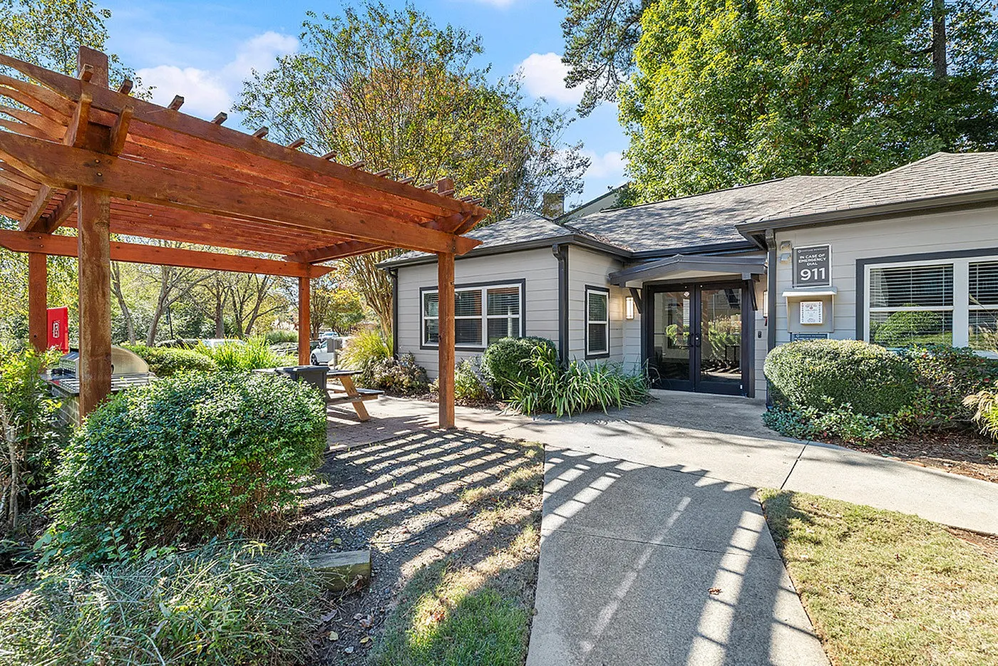 Charming apartment entrance with lush landscaping and a wooden pergola, offering a welcoming and serene atmosphere.