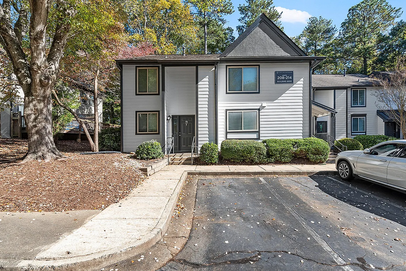 Charming apartment building with modern exterior, surrounded by lush greenery and ample parking space.