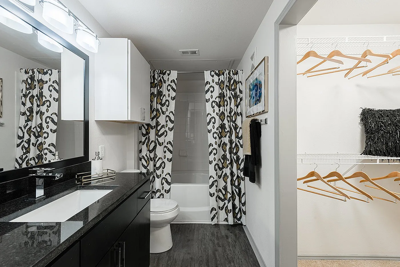 Modern bathroom with elegant black granite countertop, stylish vanity, and chic patterned shower curtains, adjacent to a spacious walk-in closet with ample hanging space.