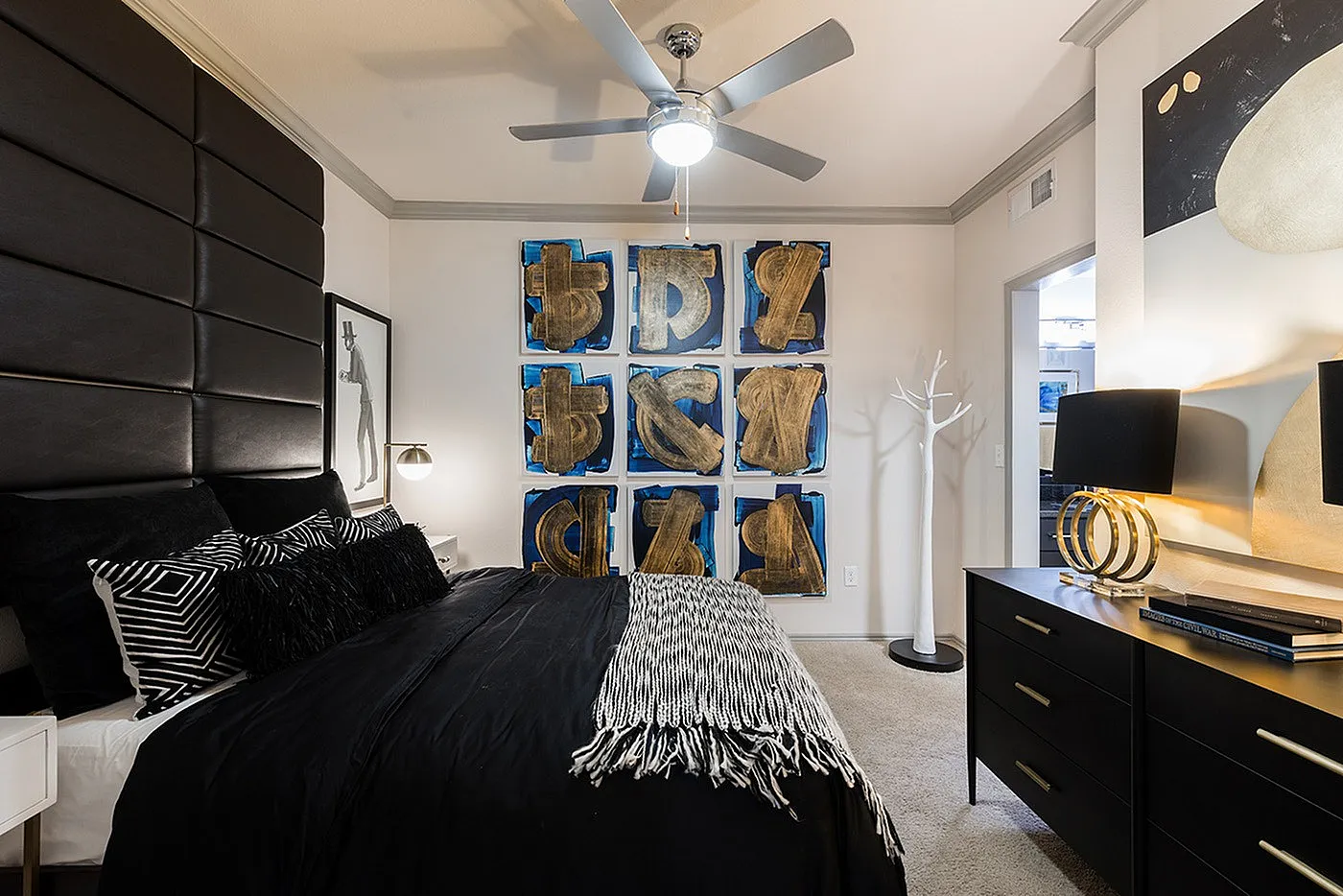 Chic bedroom with bold artwork, modern ceiling fan, and elegant black decor, exuding contemporary charm.