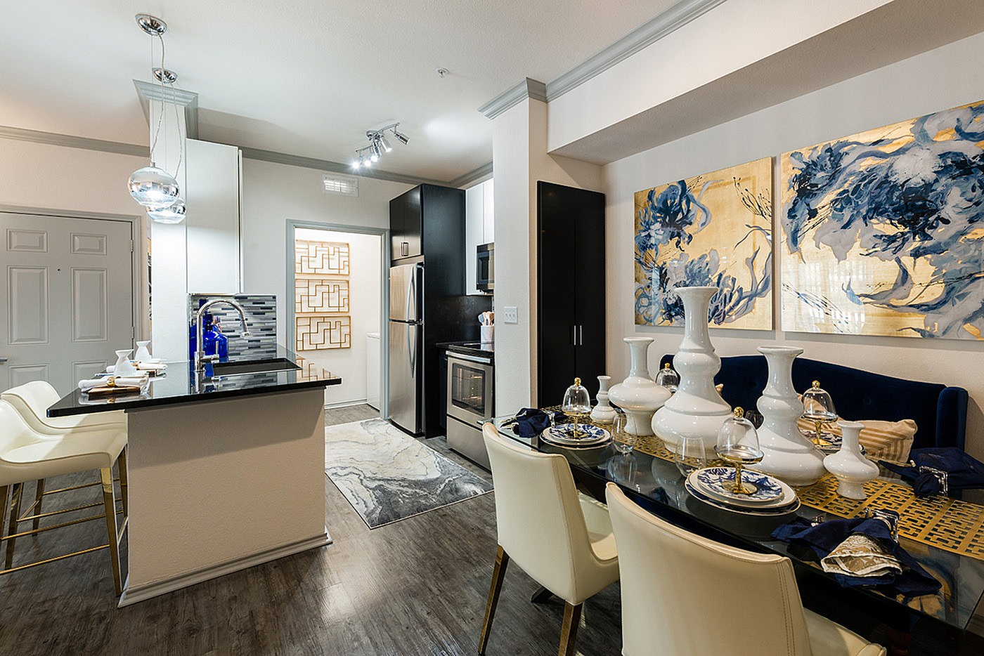 Elegant modern kitchen and dining area featuring sleek black cabinetry, stainless steel appliances, and chic pendant lighting. The stylish dining table is adorned with decorative white vases and vibrant artwork accents the walls, adding sophistication to the space.