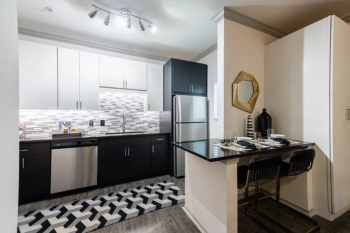 Modern kitchen with sleek black and white cabinetry, stylish mosaic backsplash, stainless steel appliances, and a cozy dining nook.