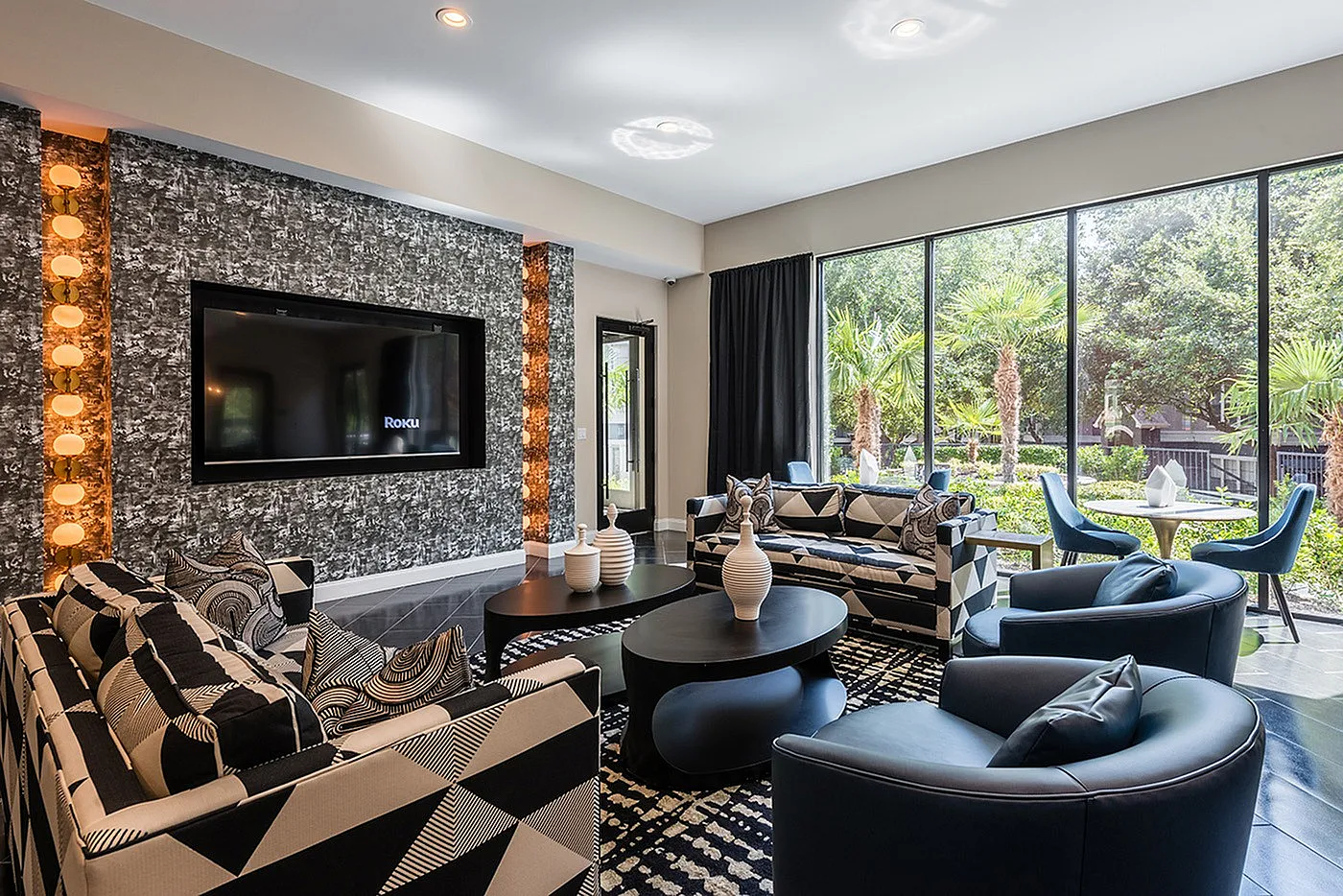Chic and modern living room with large windows, elegant geometric furniture, and lush outdoor views.