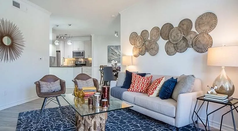 Bright and modern living room with elegant decor, featuring colorful cushions, unique wall art, and a cozy seating area leading to an open kitchen.
