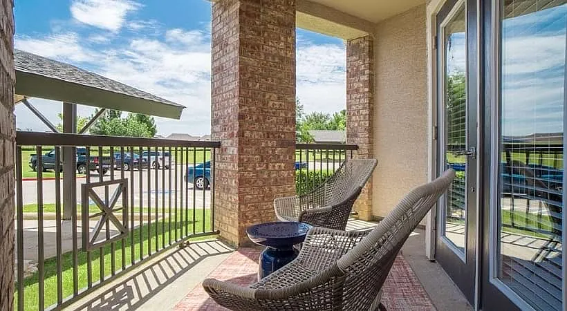 Charming apartment balcony with two stylish wicker chairs and a serene view of a green courtyard, perfect for relaxation.