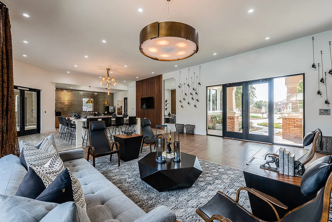 Spacious and elegant living area with modern decor, featuring a plush gray sofa, stylish seating, chic lighting, and floor-to-ceiling windows opening to a serene garden view.