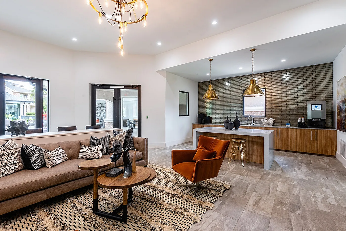 Elegant open-concept living space featuring a plush sofa, modern lighting, and a stylish kitchen with brick backsplash and gold accents.