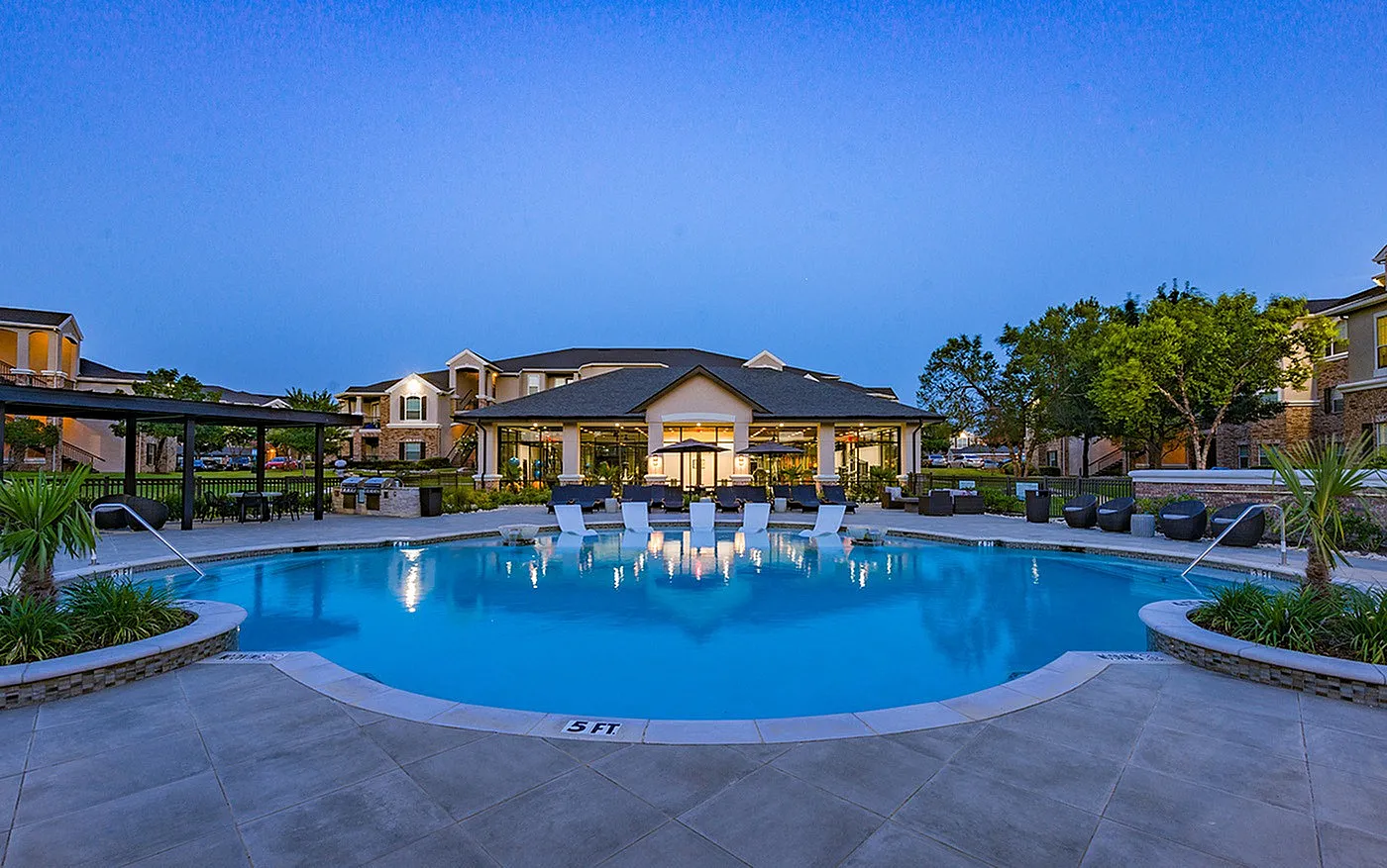 Luxurious apartment complex featuring a sparkling pool, elegant loungers, and serene landscaping at dusk.