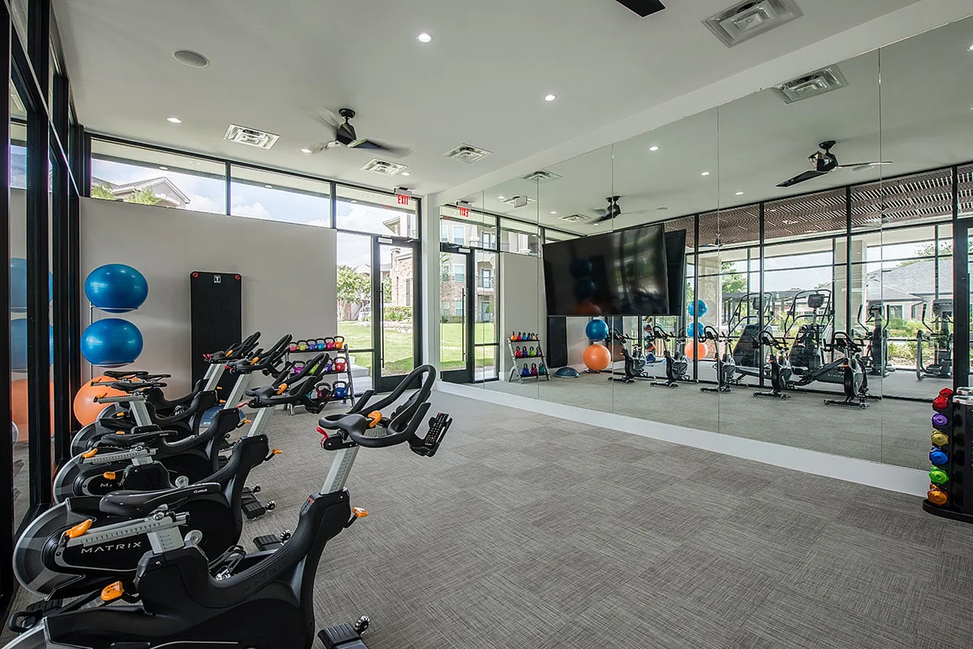 Modern gym facility with state-of-the-art stationary bikes, vibrant exercise balls, and a mirrored wall reflecting a spacious, bright workout environment.