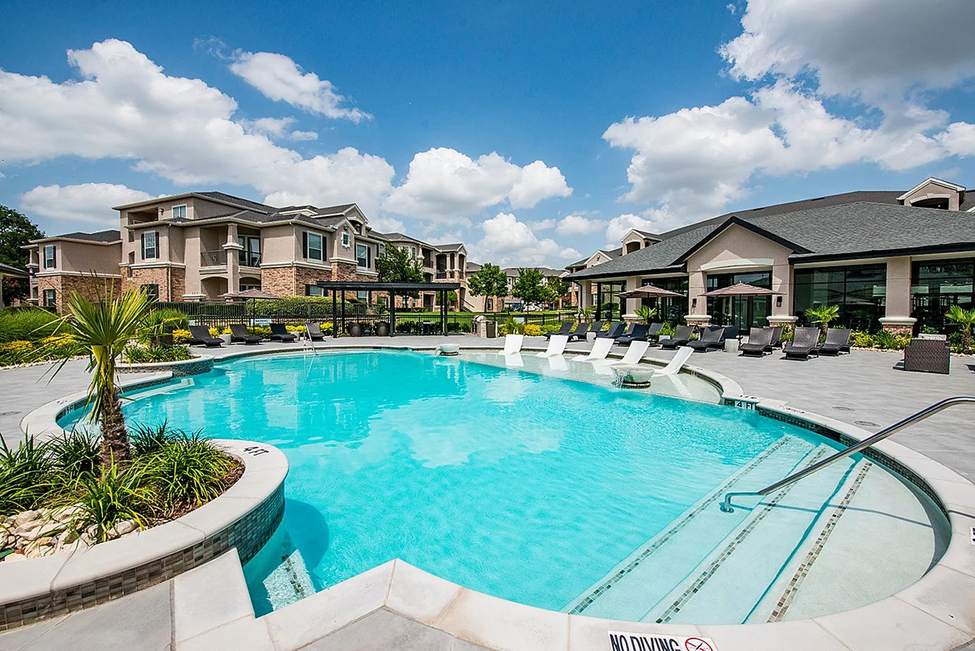 Luxurious apartment complex with a stunning outdoor pool, surrounded by lush greenery and stylish lounge chairs, perfect for relaxation and leisure.