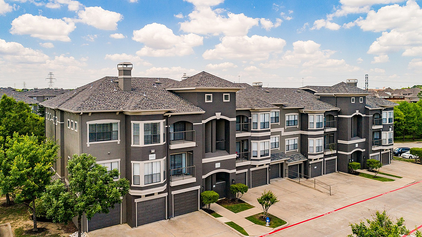 Elegant apartment complex with modern architecture and lush greenery under a bright blue sky.