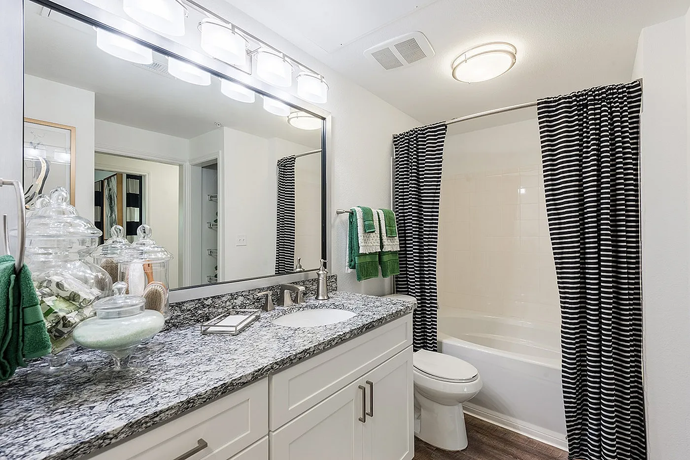 Elegant bathroom featuring granite countertop, stylish lighting, and chic striped shower curtain.