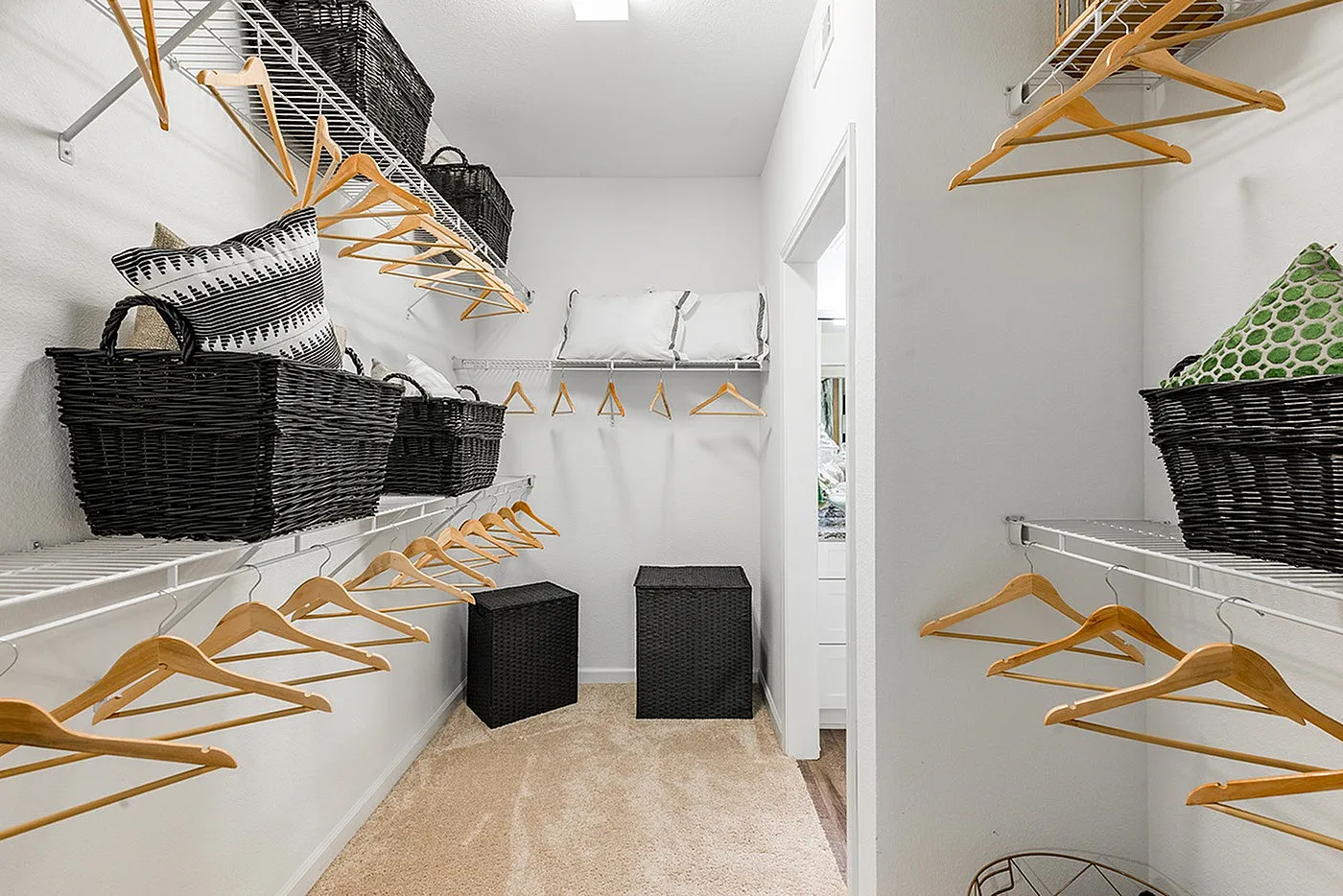 Spacious and well-organized walk-in closet featuring abundant shelving, stylish black baskets, and elegant wooden hangers, perfect for wardrobe organization.