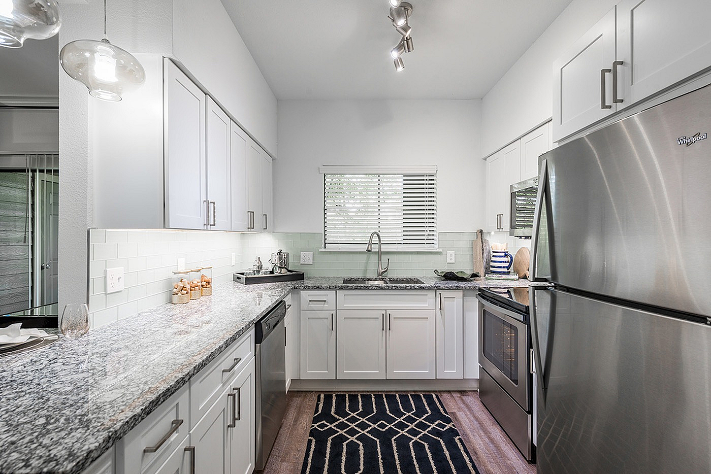 Modern kitchen with sleek white cabinetry, stainless steel appliances, granite countertops, and elegant lighting.