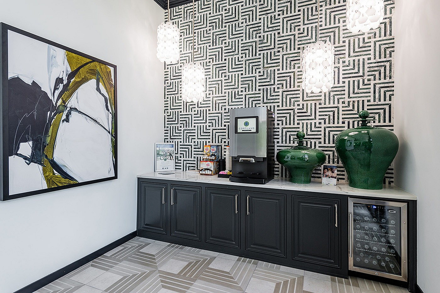 Chic coffee station with modern art and geometric wallpaper, featuring a sleek countertop, coffee machine, vibrant green vases, and wine cooler.